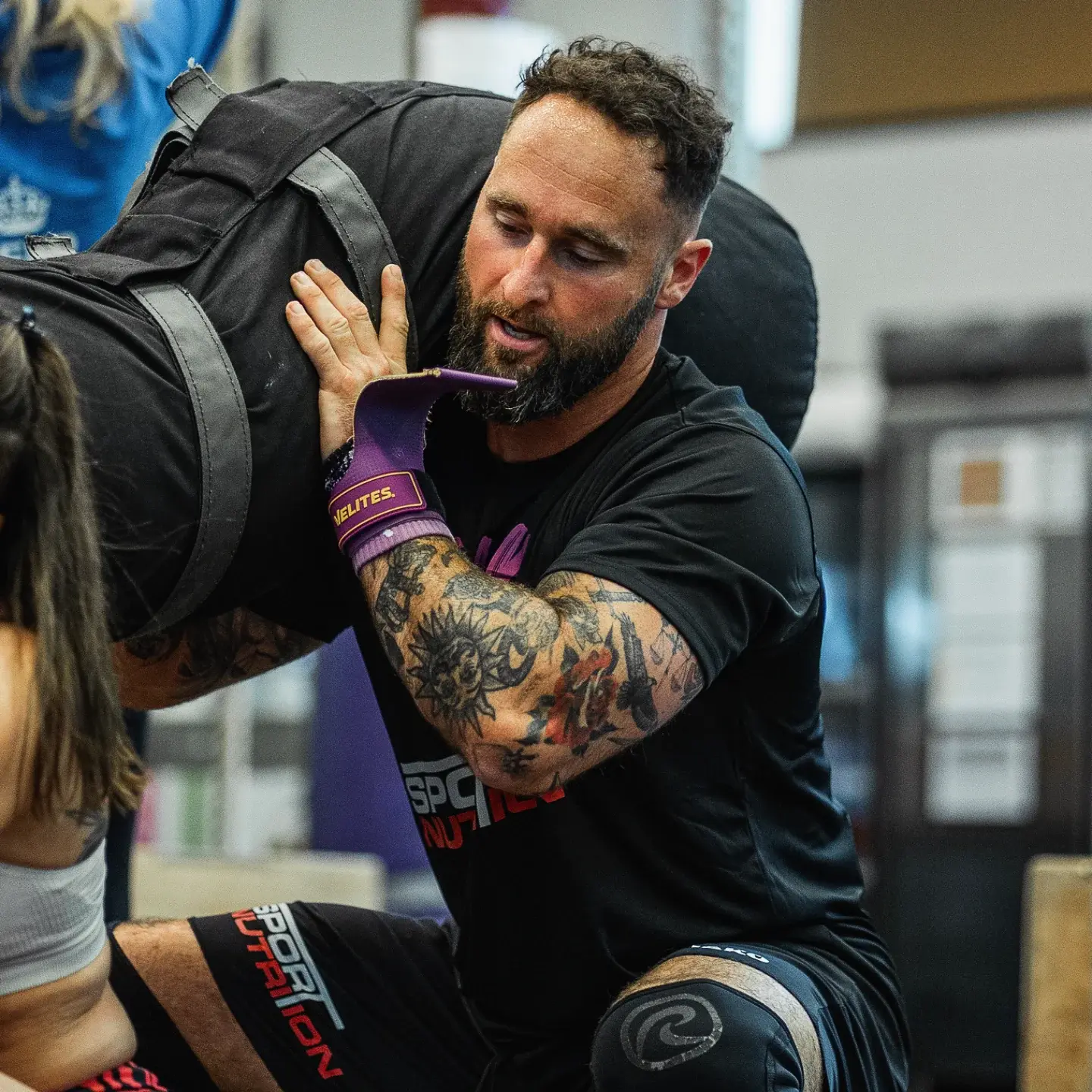 Coach guiding an athlete through a sandbag carry